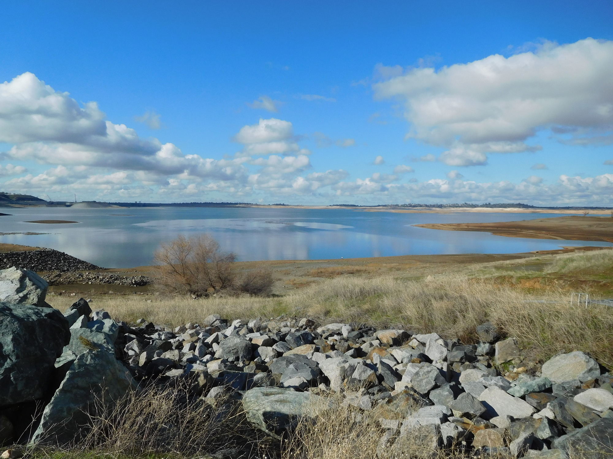 A wide view across Folsom Lake with rocky shoreline and a cloud-filled blue sky near Granite Bay, California